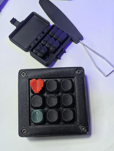 a box of caps and a macropad A macropad with a pixel heart and mlg glasses sit on a clean white background.