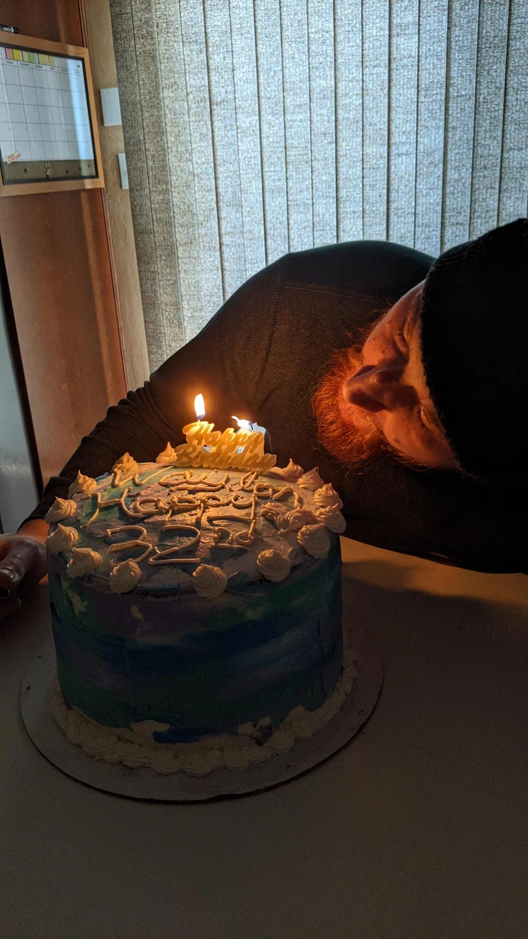 Man leaning toward lit candles on a blue cake