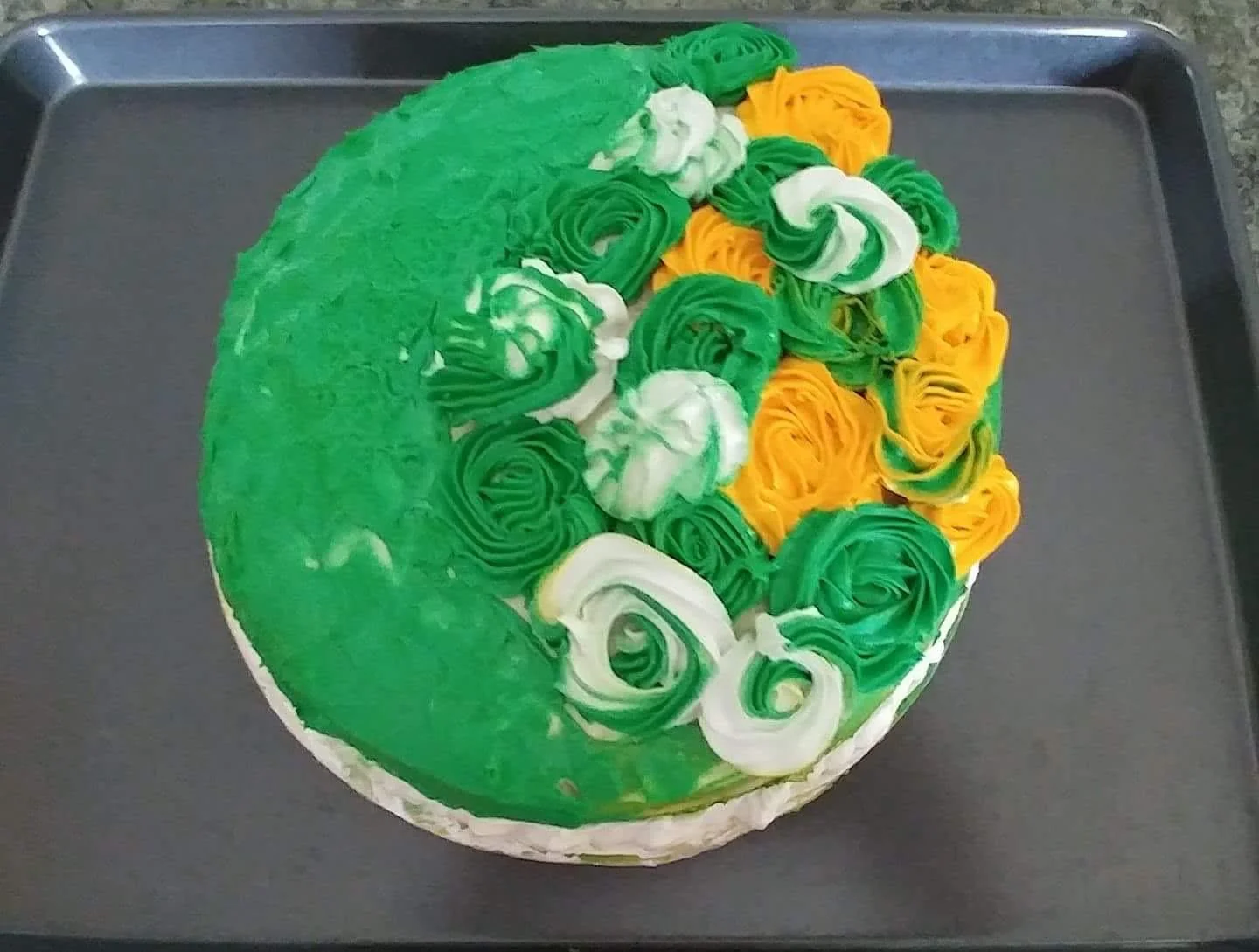 Green cake decorated with white and yellow frosting rosettes