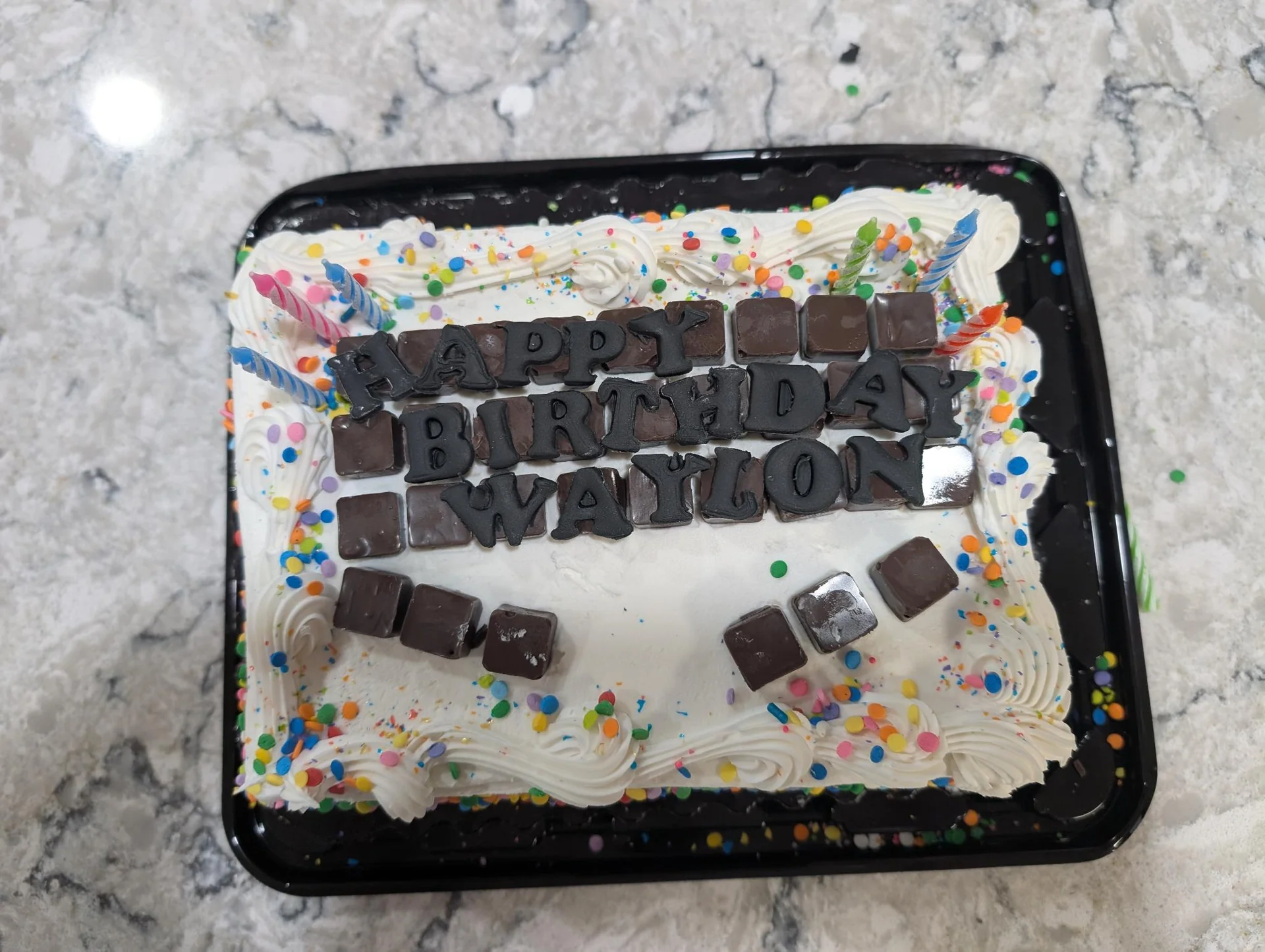 Rectangular birthday cake with dark lettering and sprinkles