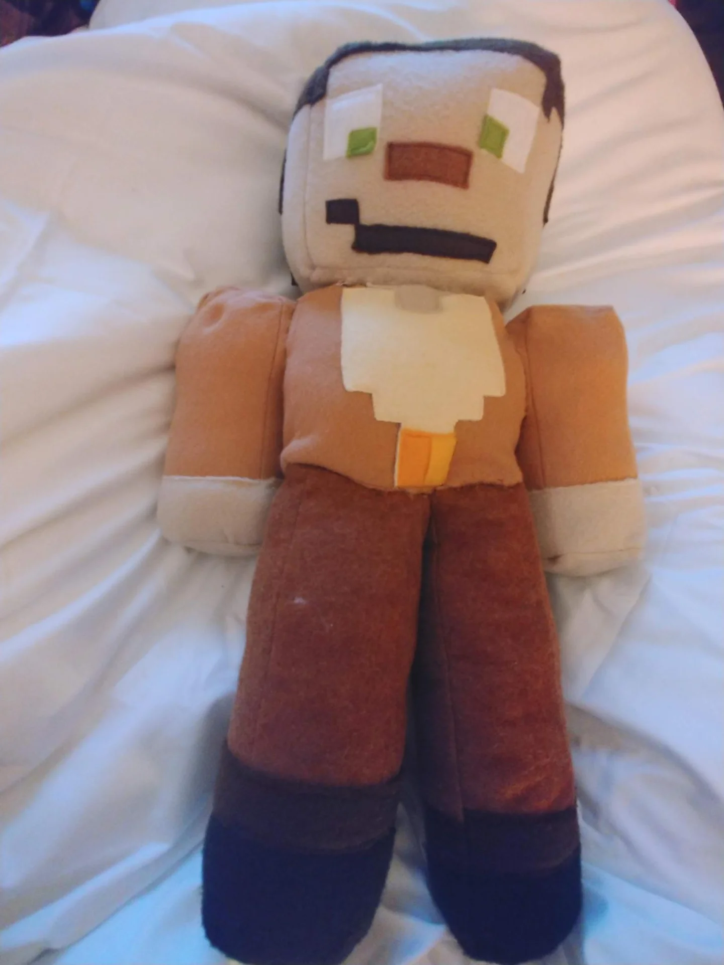 Handmade block-shaped plush character on a bed
