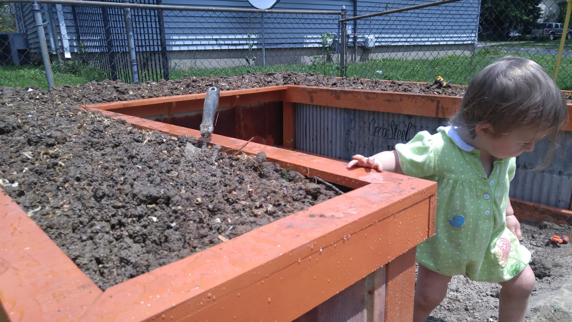 Child beside a raised garden bed filled with soil