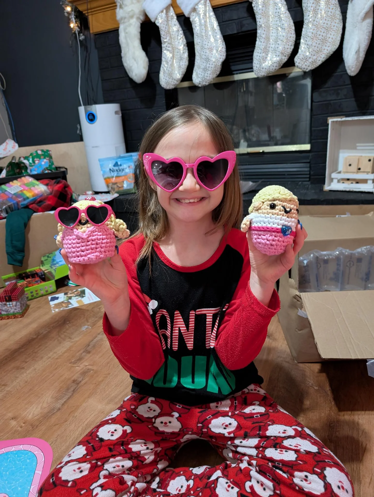 Child in sunglasses holding two crocheted cupcakes