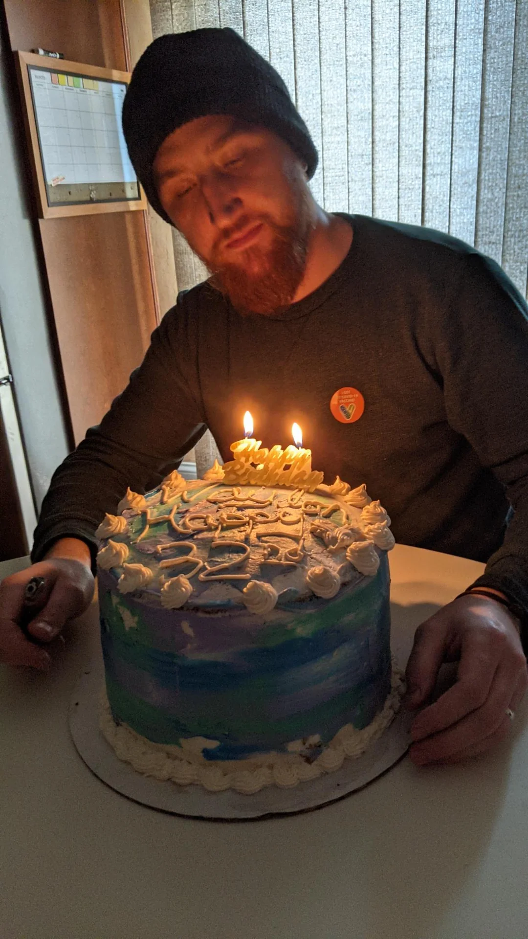 Man smiling beside a blue cake with lit candles