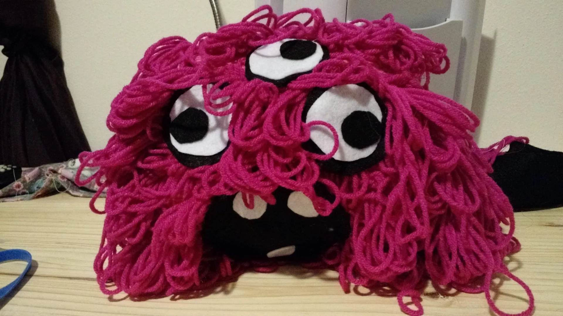 Pink yarn monster with large eyes and loose strands