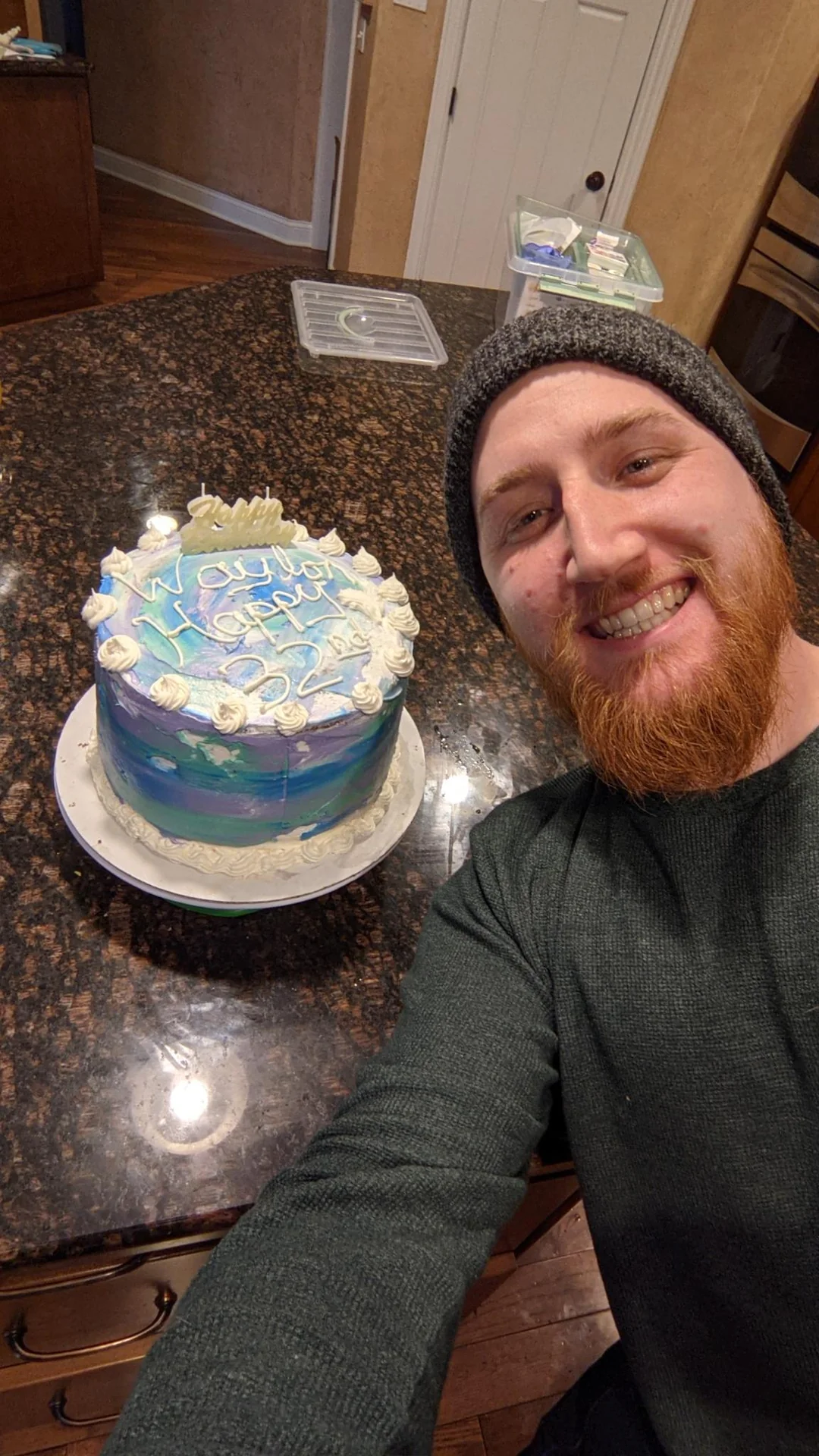 Man taking a selfie beside a blue birthday cake