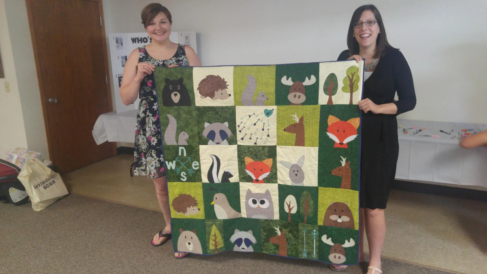 Two people holding up a woodland animal quilt