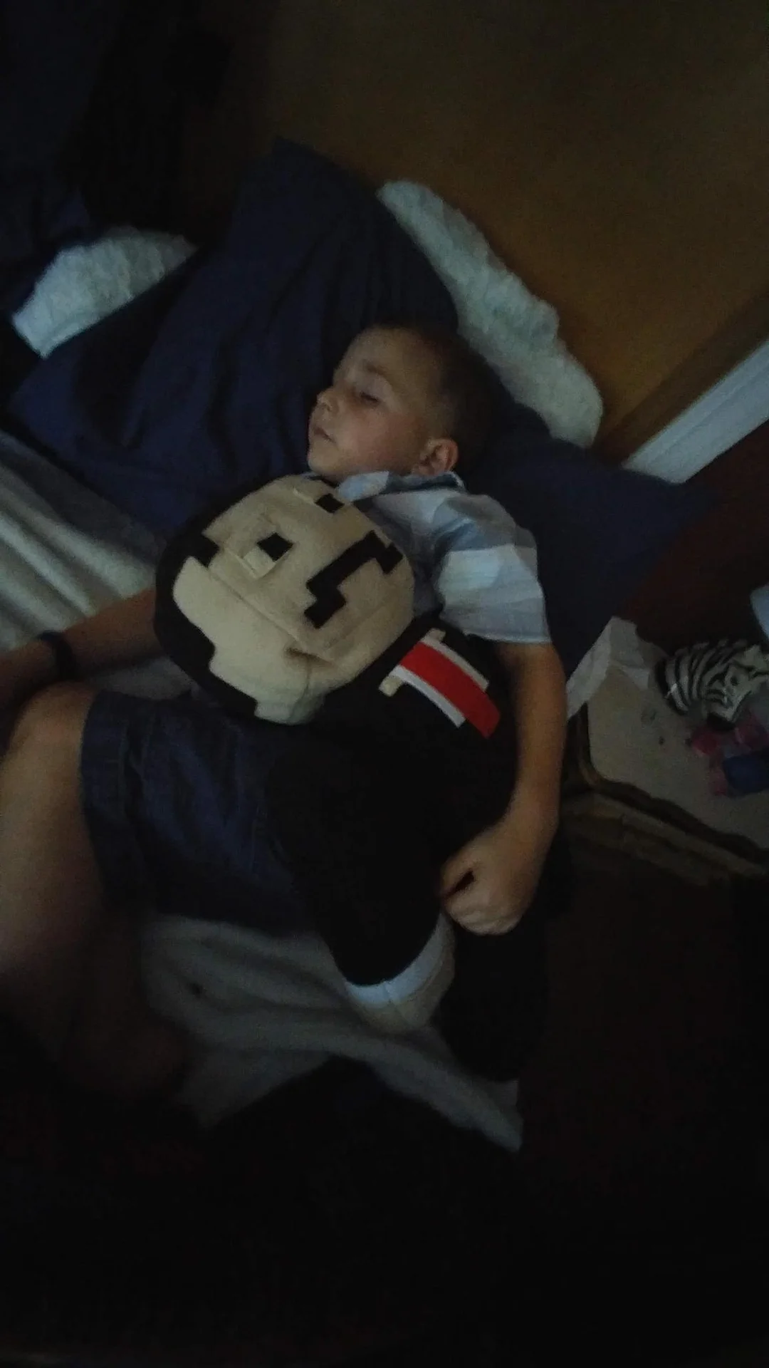 Child lying in bed and holding a block-shaped plush figure