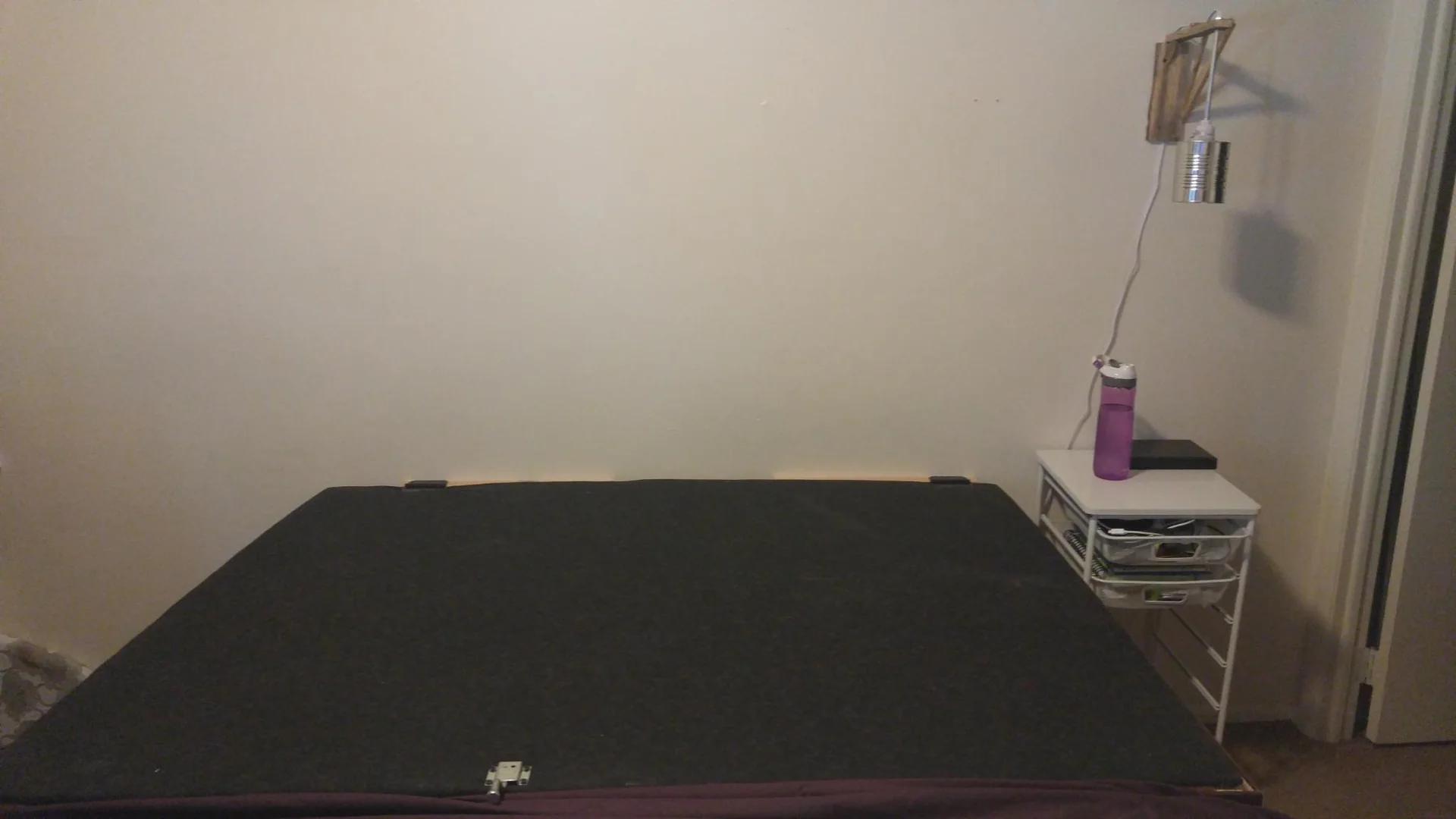 Bare bed with a dark cover and a bedside table
